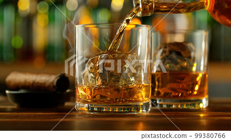 Detail of pouring whiskey into glass with ice cubes. 99380766