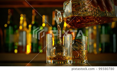 Detail of pouring whiskey into glass with ice cubes. Detail of pouring whiskey into glass with ice cubes. 99380780