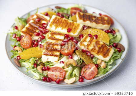 Warm salad with fried halloumi cheese, nuts (cashews and almonds), cherry tomatoes, pomegranate, orange and arugula. Traditional cheese of the Eastern Mediterranean. Selective focus, close-up. 99383710