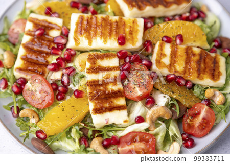 Warm salad with fried halloumi cheese, nuts (cashews and almonds), cherry tomatoes, pomegranate, orange and arugula. Traditional cheese of the Eastern Mediterranean. Selective focus, close-up. 99383711