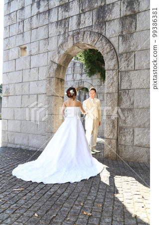 新娘和新郎穿著婚紗和燕尾服在石拱門前的外景拍攝 新娘和新郎穿著婚紗和燕尾服在石拱門前的外景拍攝 99386381
