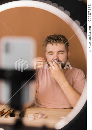 Male beauty blogger with makeup product recording video at home. Using ring lamp and smartphone. Vlog cosmetic products and diversity concept 99387188
