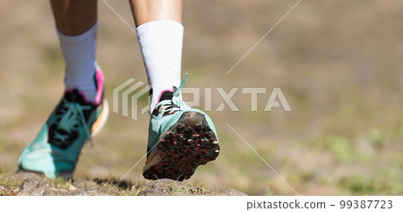 Trail running athlete exercising for fitness and health outdoors on mountain pathway, closeup of running shoes in action 99387723