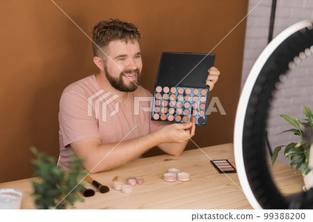 Male beauty blogger with makeup product recording video at home. Using ring lamp and smartphone. Vlog cosmetic products and diversity concept 99388200