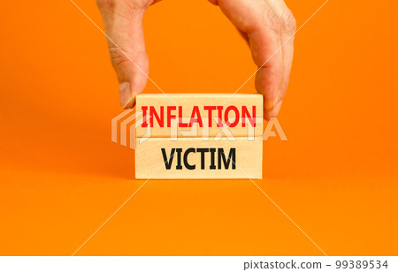 Inflation victim symbol. Concept words Inflation victim on wooden block. Beautiful orange table orange background. Businessman hand. Business inflation victim concept. Copy space. 99389534