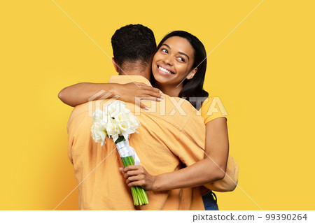 Happy young african american male giving bouquet of flowers to wife, hug isolated on yellow background Happy young african american male giving bouquet of flowers to wife, hug isolated on yellow background 99390264