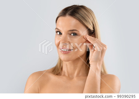 Closeup of blonde middle aged woman playing with face skin 99390295