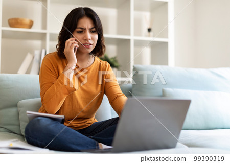 Young Arab Female Working With Laptop And Talking On Cellphone At Home 99390319