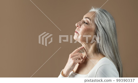 Calm mature european female with gray hair touches neck skin, enjoy treatment 99390337