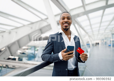 Young Black Businessman Using Smartphone And Credit Card While Standing In Airport Young Black Businessman Using Smartphone And Credit Card While Standing In Airport 99390392
