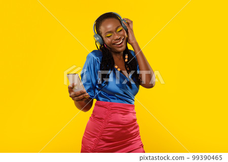 African Lady Listening Music On Smartphone Wearing Headphones, Yellow Background African Lady Listening Music On Smartphone Wearing Headphones, Yellow Background 99390465