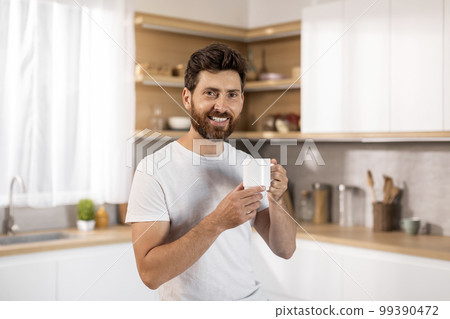 Smiling attractive adult caucasian man in white t-shirt enjoy cup of fresh coffee and spare time Smiling attractive adult caucasian man in white t-shirt enjoy cup of fresh coffee and spare time 99390472