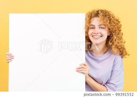 Smiley woman with curly hair holding a blank panel Smiley woman with curly hair holding a blank panel 99391552
