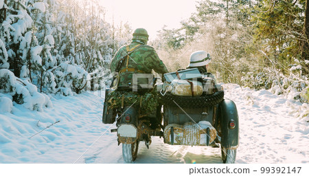 Re-enactors Dressed As World War II German Wehrmacht Infantry Soldiers Driving Old Tricar, Three-wheeled Motorcycle in Winter Snowy Forest 99392147