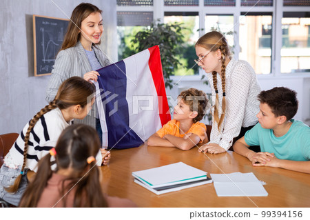 Geography lesson in school class - teacher talks about France, holding flag in his hands Geography lesson in school class - teacher talks about France, holding flag in his hands 99394156