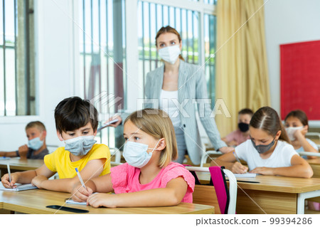 Preteen pupils in protective masks studying in classroom with female teacher 99394286