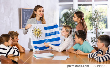 Teacher showing Uruguay flag to group of schoolchildren Teacher showing Uruguay flag to group of schoolchildren 99394380