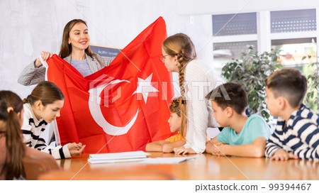 Cheerful young woman teacher demonstrating Turkish flag for schoolkids preteens during lesson of geography in auditory Cheerful young woman teacher demonstrating Turkish flag for schoolkids preteens during lesson of geography in auditory 99394467