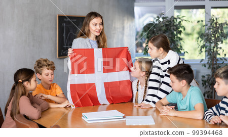 School teacher tells students about Denmark and holds a Denmark flag in hands. School teacher tells students about Denmark and holds a Denmark flag in hands. 99394468