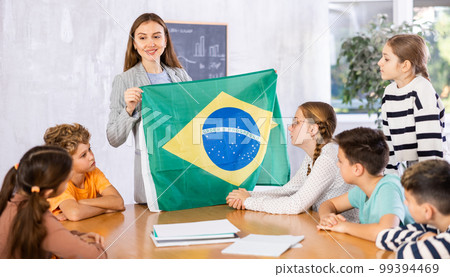 Teacher holds the flag of Brazil in her hands and tells the students about country Teacher holds the flag of Brazil in her hands and tells the students about country 99394469