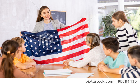 Geography lesson in school class - teacher talks about United States of America, holding flag in his hands Geography lesson in school class - teacher talks about United States of America, holding flag in his hands 99394489