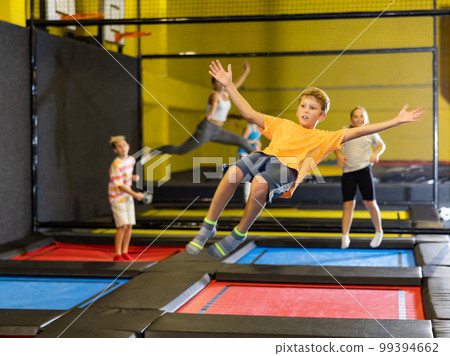 Smiling school-age boy having fun, jumping and indulging on trampolines in entertainment center. Active leisure concept 99394662