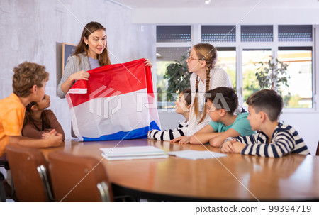 Teacher holds the flag of Netherlands in her hands and tells students about this country 99394719