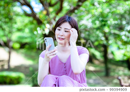 A woman in a dress using a smartphone in a fresh green park 99394909