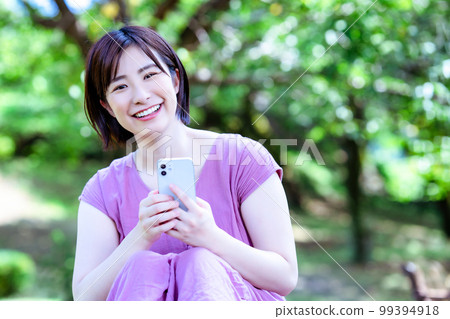 A woman in a dress using a smartphone in a fresh green park A woman in a dress using a smartphone in a fresh green park 99394918