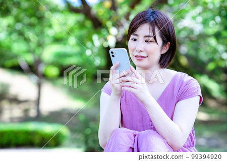 A woman in a dress using a smartphone in a fresh green park 99394920