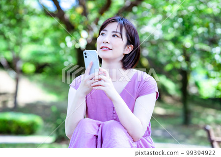 A woman in a dress using a smartphone in a fresh green park 99394922
