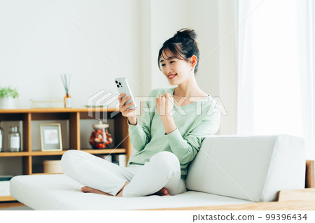 年輕女子在客廳看智慧型手機 年輕女子在客廳看智慧型手機 99396434