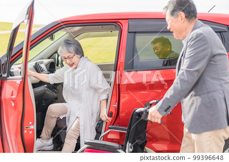 An elderly woman on a wheelchair after getting off the car and a man assisting (transfer) An elderly woman on a wheelchair after getting off the car and a man assisting (transfer) 99396648