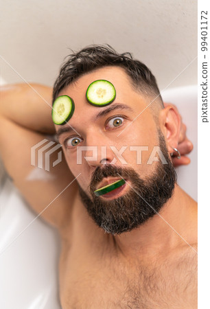 Funny man with cucumber on his face in bath at home 99401172