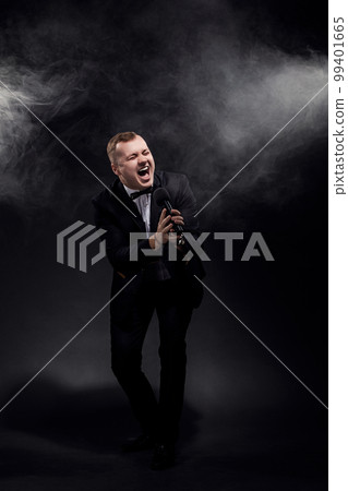 Full length of emotional man singing in microphone on black background, singer, actor, leading  99401665