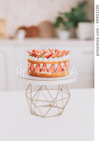Mousse cake with strawberries on a geometric stand in front of the kitchen 99403500