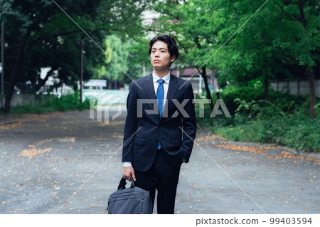 A businessman in a suit walking on a green road 99403594
