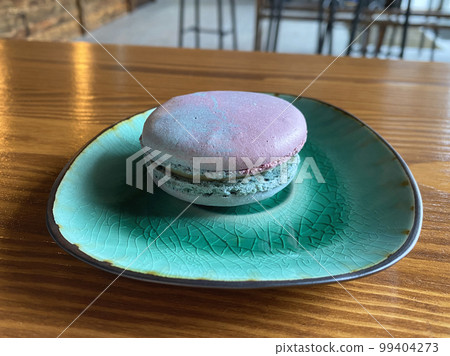 One pink and blue space-colored macaroons on a green plate on a table in a cafe. One pink and blue space-colored macaroons on a green plate on a table in a cafe. 99404273