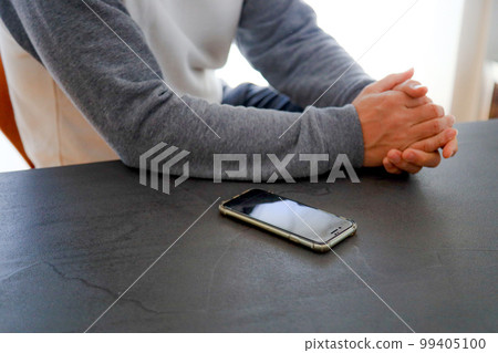 A man sitting on a chair with his arms folded, a smartphone, a table and a person 99405100