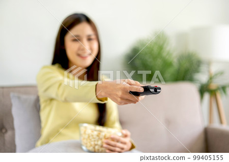 Young asian woman is watching movie on television and holding remote control to switching channel while Young asian woman is watching movie on television and holding remote control to switching channel while 99405155
