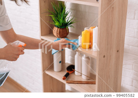 Lady with a rag in her hands sprays detergent on the cabinet shelves Lady with a rag in her hands sprays detergent on the cabinet shelves 99405582