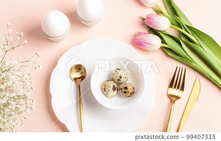 Festive Easter table decoration idea with eggs, spring flowers, golden cutlery, beautiful plates. Holiday image in gentle peach color. Top view, flat lay. Festive Easter table decoration idea with eggs, spring flowers, golden cutlery, beautiful plates. Holiday image in gentle peach color. Top view, flat lay. 99407315