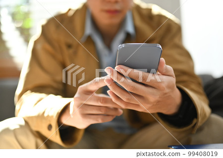 Selective focused on hands. Man chatting online in social network on smart phone while sitting on couch at home 99408019