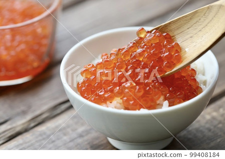 Chopsticks holding salmon roe marinated in soy sauce. A generous amount of salmon roe is placed on rice. 99408184