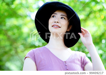 A one-piece woman wearing a hat refreshing in a fresh green park 99409217