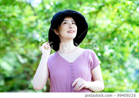A one-piece woman wearing a hat refreshing in a fresh green park 99409218