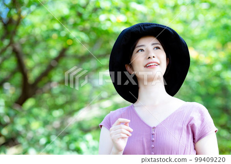 A one-piece woman wearing a hat refreshing in a fresh green park A one-piece woman wearing a hat refreshing in a fresh green park 99409220