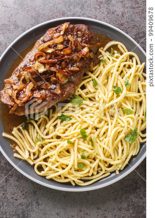 Austrian Steak Zwiebelrostbraten With Crispy Onions and spaetzle pasta closeup on the plate. Vertical top view Austrian Steak Zwiebelrostbraten With Crispy Onions and spaetzle pasta closeup on the plate. Vertical top view 99409678