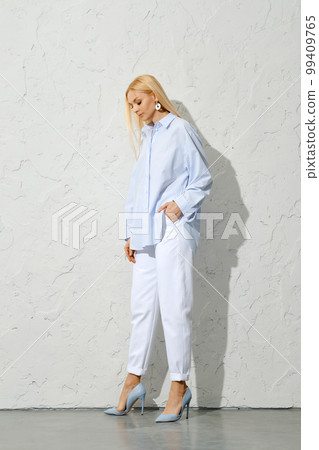 Pensive blonde woman in blue shirt, white jeans and stilettos looking down Pensive blonde woman in blue shirt, white jeans and stilettos looking down 99409765
