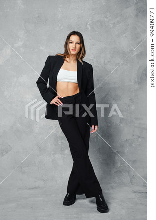 Full length portrait of young woman in black pantsuit and white top crossing legs Full length portrait of young woman in black pantsuit and white top crossing legs 99409771